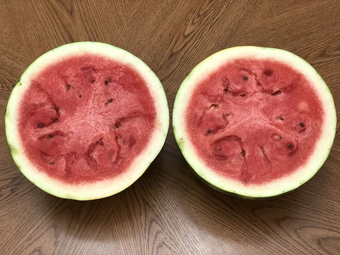 도마 위에서 잘 익은 수박을 반으로 가르자 붉은 속과 검은 씨가 드러나는 장면, 감춰졌던 결과가 밝혀지는 수박 자르는 꿈의 의미를 보여 주는 이미지